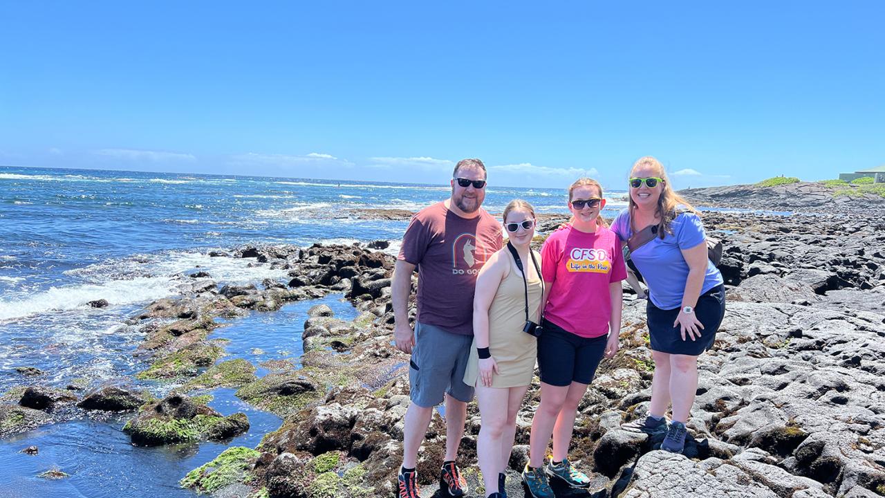 Eric O'Brien posing with family at a rocky beach shore.