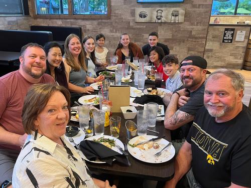 Eric O'Brien at a restaurant table with several other people. Everyone is faced toward the camera and smiling.